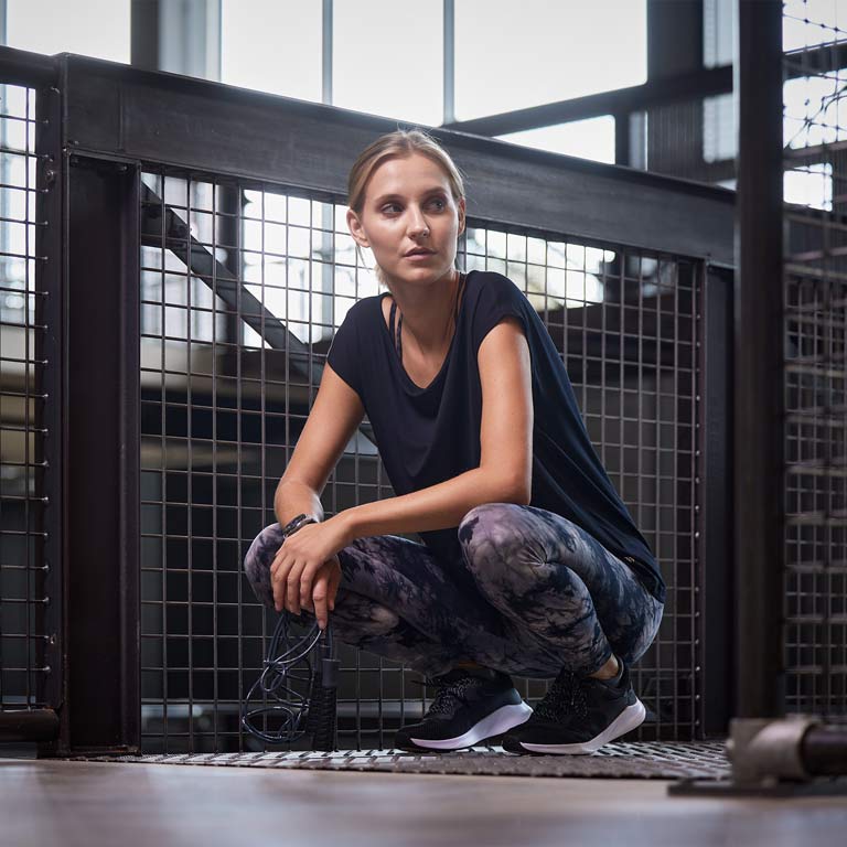 Eine Frau die in einer Hocke sitzt, mit einem Sportoutfit und Fitnessschuhen