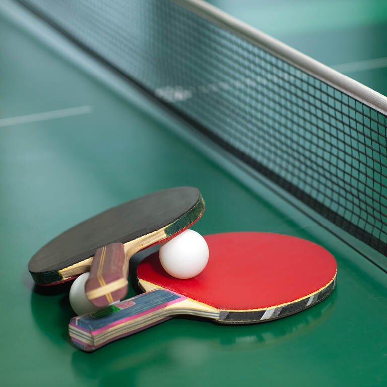 Zu sehen ist eine Tischtennisplatte mit zwei Schlägern und einem Tischtennisball