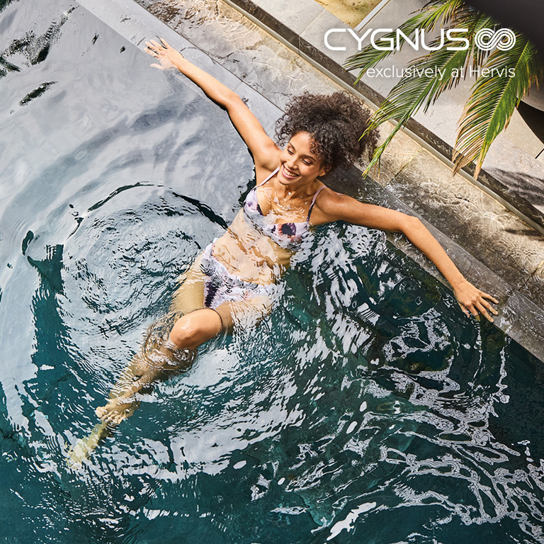Eine Person liegt entspannt im Wasser eines Pools und hält sich mit beiden Armen am Beckenrand fest. Rechts oben im Bild befindet sich das CYGNUS‑Logo mit dem Zusatz „exclusively at Hervis“.