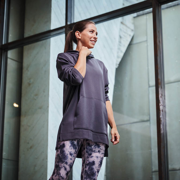 Eine Frau die eine lila-grauen Pullover mit einer Leggings trägt