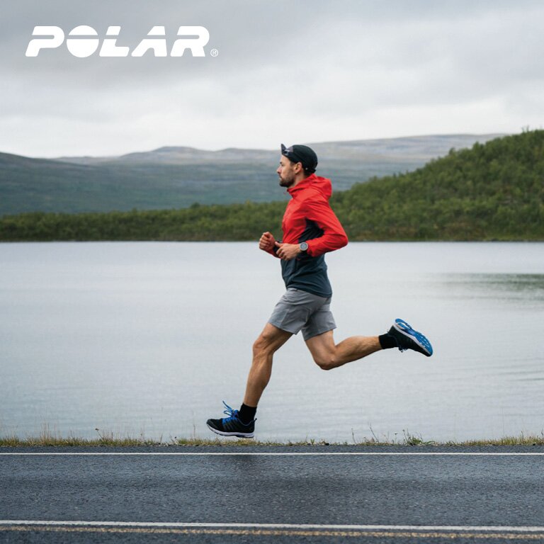 Polar Ein Mann der mit seinem Laufoutfit und seiner Polar Sportuhr neben einem See läuft