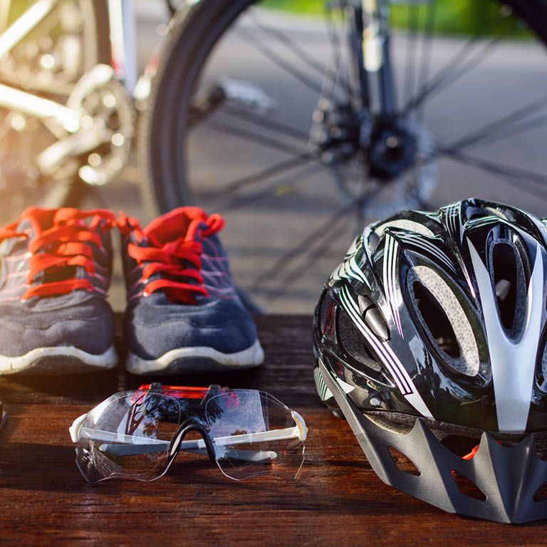 Zu sehen sind ein Fahrradhelm, eine Sonnenbrille, Sportschuhe und ein Fahrrad