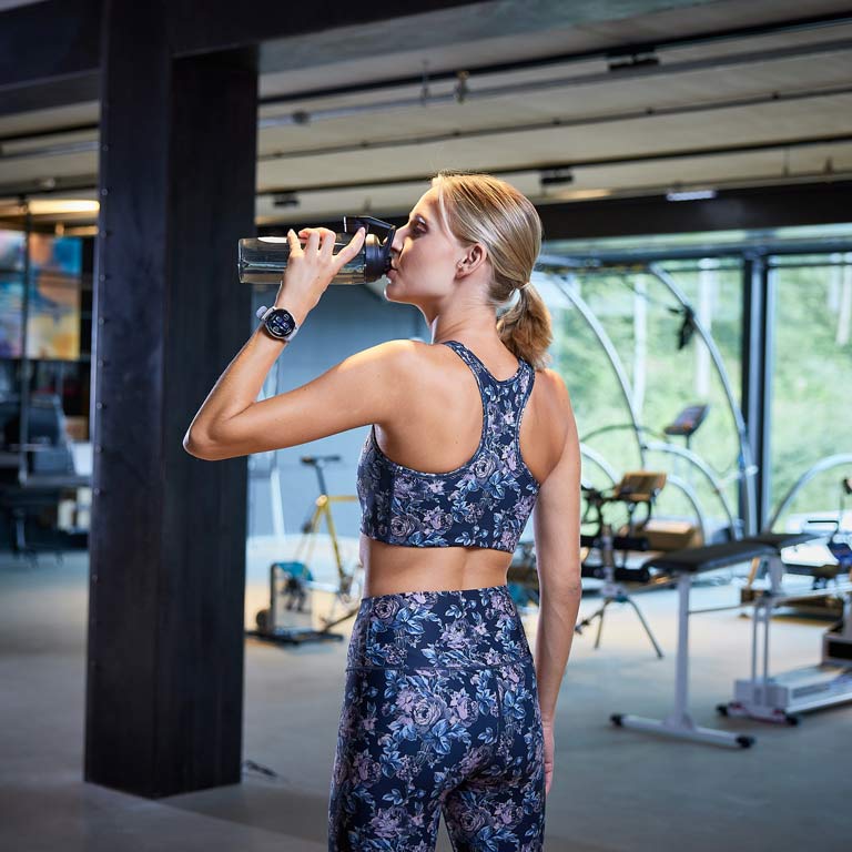 Eine Frau die eine Sportuhr am Handgelenk trägt und aus ihrer Trinkflasche trinkt