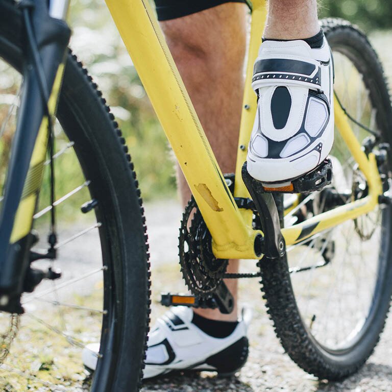Zu sehen sind weiße Radschuhe auf einem gelben Fahrrad