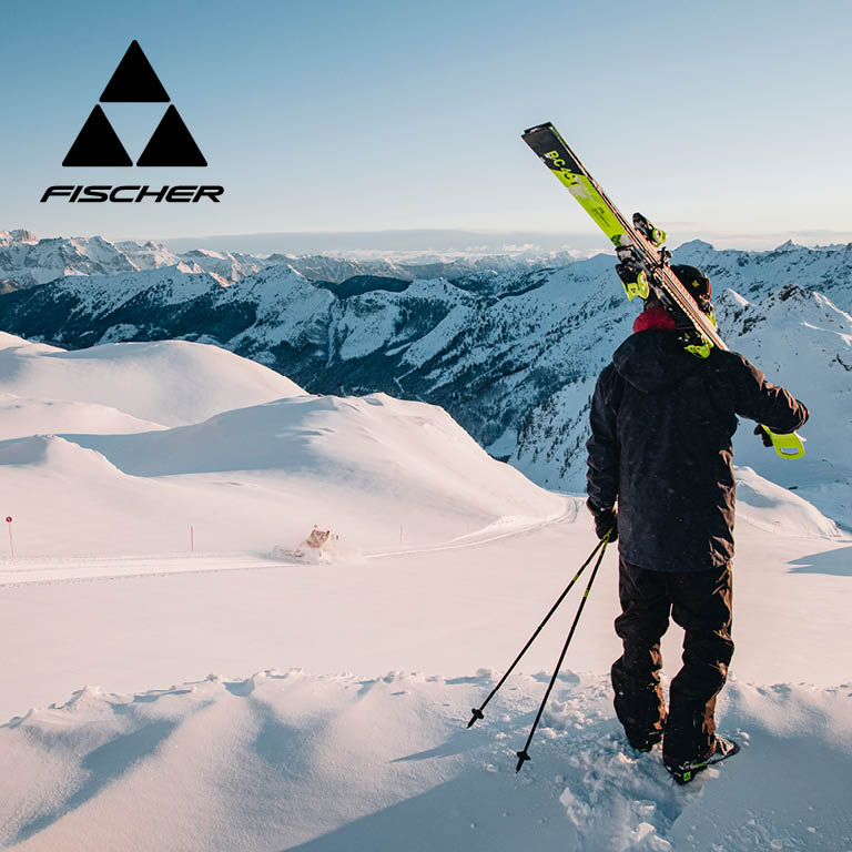 Fischer Ein Mann der mit seinen Ski durch den Schnee geht und auf die Berglandschaft blickt
