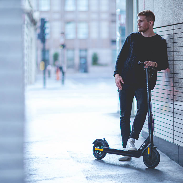 EIn Mann der an einer Wand lehnt auf seinem E-Scooter