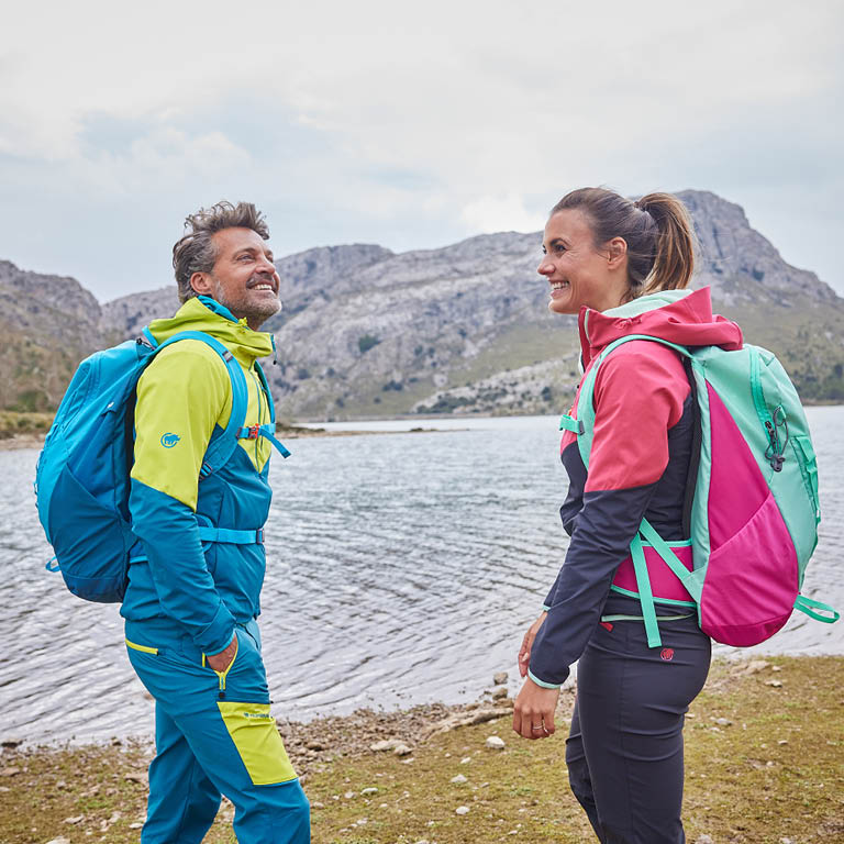 EIn Mann und eine Frau die an einem See mit Wanderbekleidung stehen und lachen