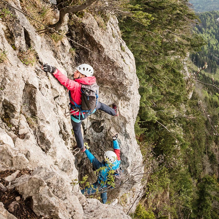 Zu sehen sind zwei Personen die einen Berg hinauf klettern