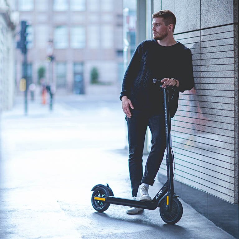 EIn Mann der an einer Wand lehnt auf seinem E-Scooter
