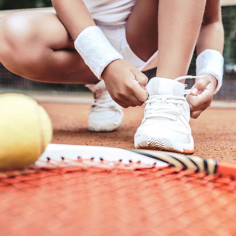 Eine Frau die sich am Tennisplatz ihre Tennisschuhe zubindet