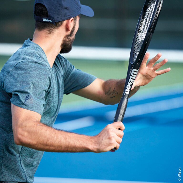 Ein Mann der mit einem schwarzen Wilson Tennisschläger spielt