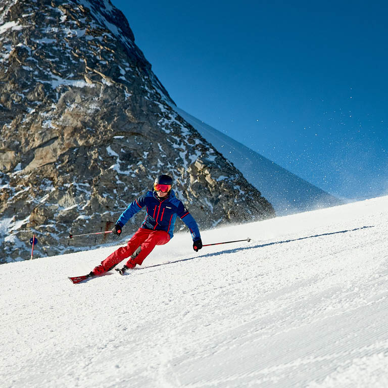 Ein Mann der in Skiausrüstung die Piste runterfährt