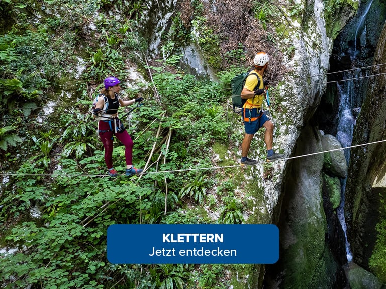 Ein Mann und eine Frau gehen gesichert über eine Schlucht in den Bergen Klettern Jetzt Entdecken