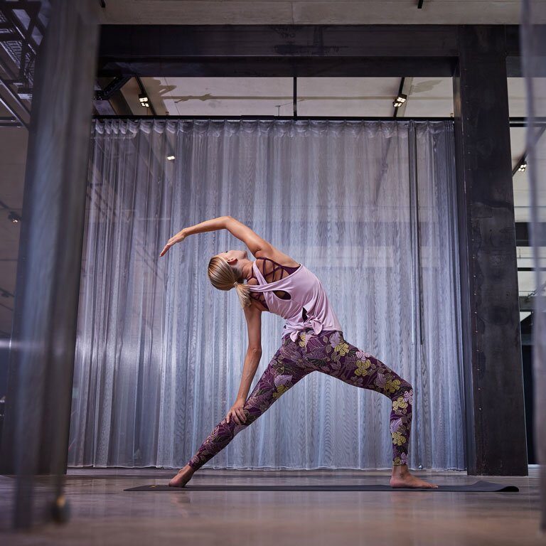 Eine Frau die Yoga macht und eine Leggings und eine lilanes Top trägt